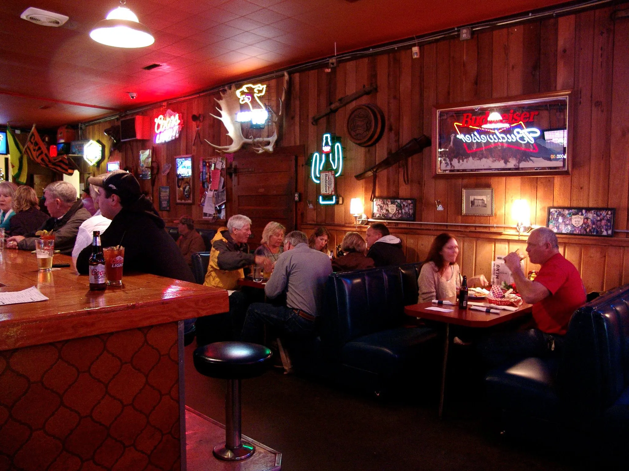Red wood-paneled room with neon signs, vinyl booth seating, and patrons in the background.