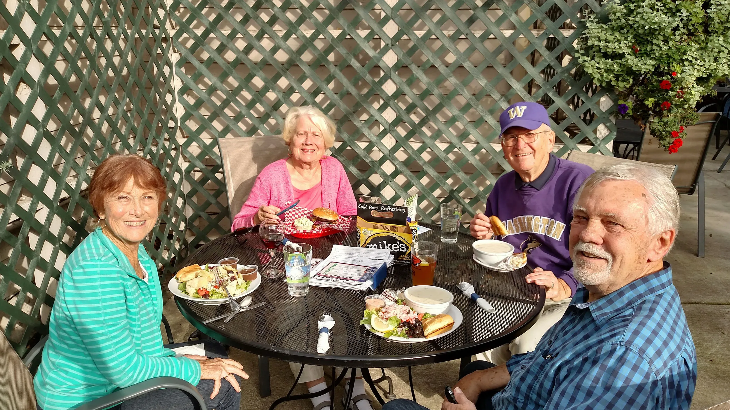 Sunny afternoon on the patio, four friends around a black table eating burgers and fries.